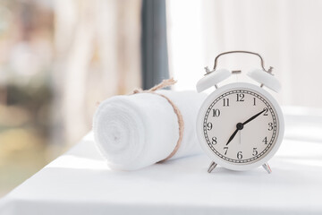Alarm clock, white towels on white wooden table with copy space blurred background. Beauty concept...