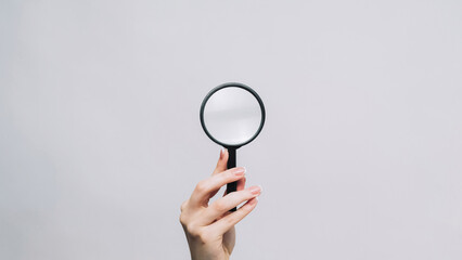 Magnifying glass. Zooming tool. Woman hand exploring empty space with loupe examining information isolated on gray background.