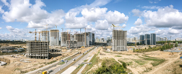 high-rise apartment buildings under construction and working cranes against blue cloudy sky. aerial...