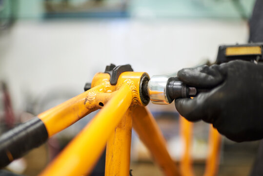 Maintenance of a bicycle: hands of an unrecognizable person using gloves disassembling an orange bike at his repair shop.