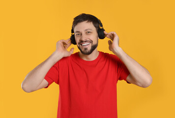 Happy man in headphones enjoying music on orange background