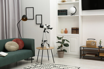 Tripod with modern telescope on table in living room