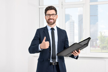 Fototapeta premium Handsome real estate agent with documents showing thumbs up indoors