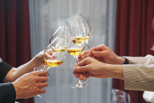 Fun company of people clink glasses, drinking white wine, focus on hands cheers, symbolizing celebration, drink degustation