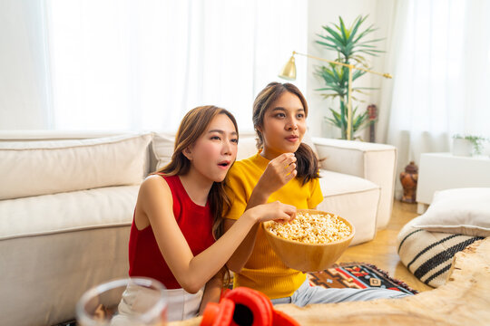 Young Asian woman friends watching movie on television together in living room at home. Attractive girl enjoy and fun indoor activity lifestyle spending time together on summer holiday vacation.