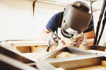 Male in face mask welds with argon-arc welding