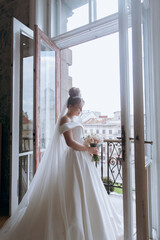 Morning preparations of a beautiful, sexy bride in a bathrobe on the balcony and on the sofa, where she puts on shoes in a wedding dress