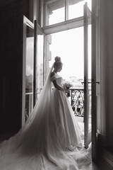 Morning preparations of a beautiful, sexy bride in a bathrobe on the balcony and on the sofa, where she puts on shoes in a wedding dress