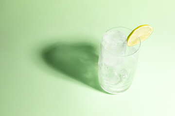 Cold glass full of ice with a lime, ready to serve light green with cast shadow.