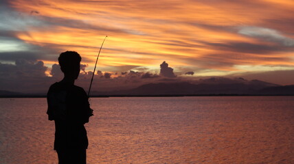 silhouette of a fisherman with a fishing rod in the lake at sunset