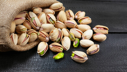 Pistachio in nutshell on black wooden rustic backdrop in burlap sack, composition of pistachios great for healthy and dietary nutrition. Concept of nuts