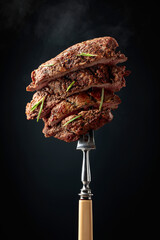Grilled beef steak on a fork sprinkled with rosemary.