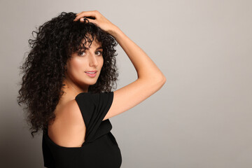 Naklejka premium Beautiful young woman with long curly hair on light grey background. Space for text
