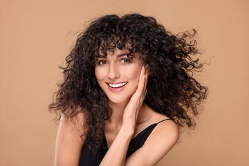 Beautiful young woman with long curly hair on beige background