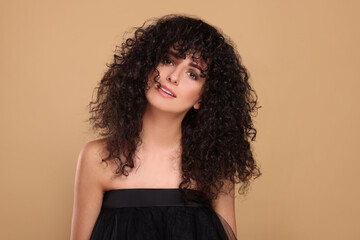 Beautiful young woman with long curly hair on beige background