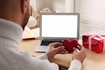 Valentine's day celebration in long distance relationship. Man holding red wooden heart while...