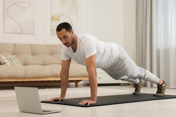Fototapeta premium Man doing morning exercise on fitness mat near laptop at home