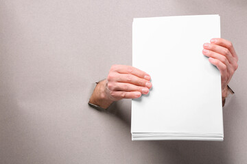 Man holding sheets of paper through holes in white paper, closeup. Mockup for design
