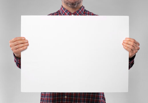 Man Holding Sheet Of Paper On Grey Background, Closeup. Mockup For Design