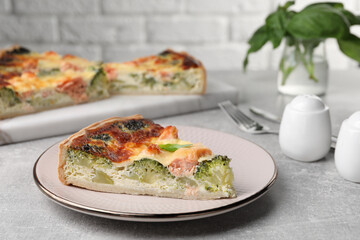 Piece of delicious homemade quiche with salmon and broccoli on light grey table