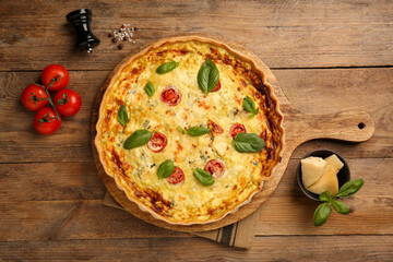 Delicious quiche with cheese, tomatoes and basil on wooden table, flat lay