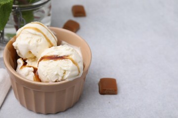 Scoops of ice cream with caramel sauce and candies on light grey table, closeup. Space for text