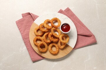 Board with tasty ketchup and onion rings on marble table, top view