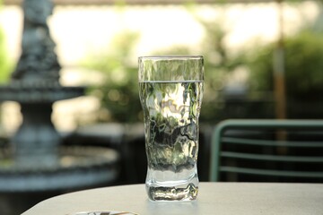 Glass of fresh water on light grey table outdoors