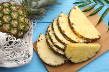Whole and cut ripe pineapples on light blue wooden table, flat lay