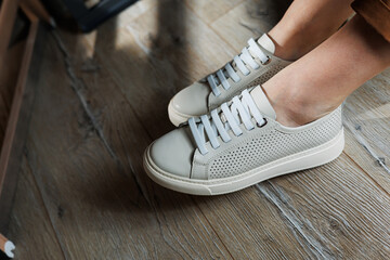 Slender female legs in pants close-up in beige casual sneakers. Women's leather shoes.