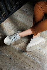 Slender female legs in pants close-up in beige casual sneakers. Women's leather shoes.