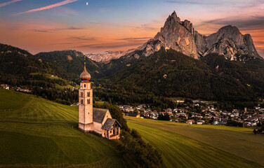 Seis am Schlern, Italy - Aerial panoramic view of St. Valentin Church and famous Mount Sciliar mountain at background with colorful sunset sky and warm sunlight at South Tyrol on a summer afternoon