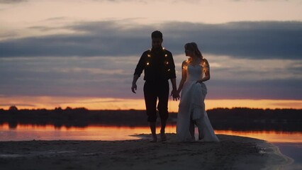 Newlyweds Walking On Beach After Sunset, Full-Length Portrait Against Red Horizon, Groom And Bride