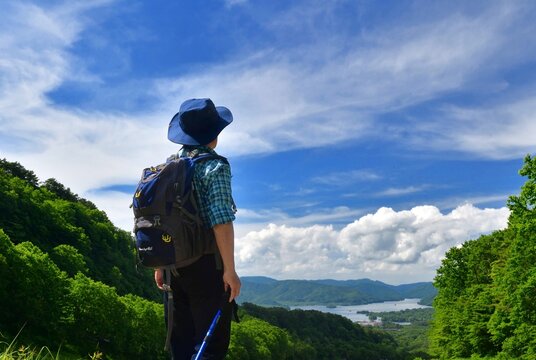 青空と緑の高原を歩く男性
