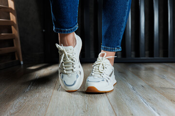Slender female legs close-up in jeans and white sneakers made of genuine leather.