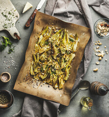 Roasted fennel topped with nuts and herbs on baking sheet on kitchen table with ingredients and...