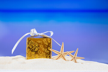 Golden packed gift box with yellow stars at tropical ocean beach. Christmas, New Year, birthday...