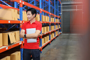 Portrait of warehouse workers young asian man standing and using computer while looking at camera and controlling stock and inventory in retail warehouse logistics, distribution center