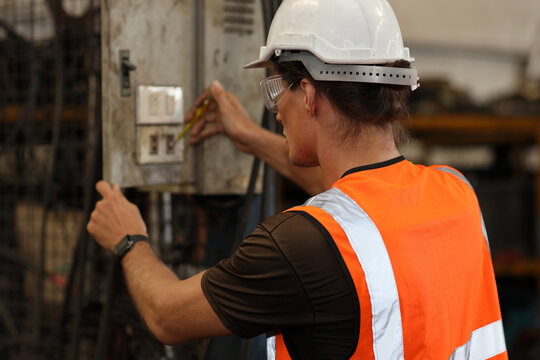 Technician engineer or worker man in protective suit standing and fixing electricity plug while controlling or maintenance operation work lathe metal machine at heavy industry manufacturing factory