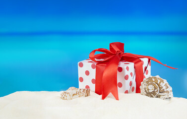 White-red gift box with polka dots with bow on sandy beach with starfish and seashell. Sale....