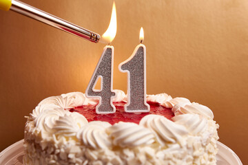 A candle in the form of the number 41, stuck in a festive cake, is lit. Celebrating a birthday or a...