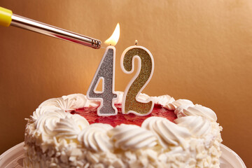 A candle in the form of the number 42, stuck in a festive cake, is lit. Celebrating a birthday or a...