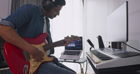 Asian musician recording electric guitar in digital studio at home. A composer is using modern equipment to help create a melody.