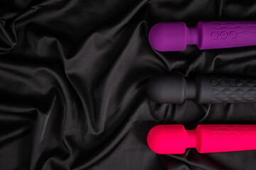 Three colored dildos on a black silk sheet. 
