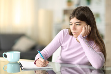 Distracted teen writing on notebook at home