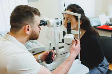 Examination of vision on modern ophthalmological equipment. Eye examination of a woman at an ophthalmologist's appointment using microscopes. Vision treatment at an ophthalmologist appointment - obrazy, fototapety, plakaty
