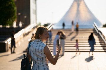 A young woman stands in the square opposite the Khan-Shatyr shopping center in Astana. - obrazy, fototapety, plakaty