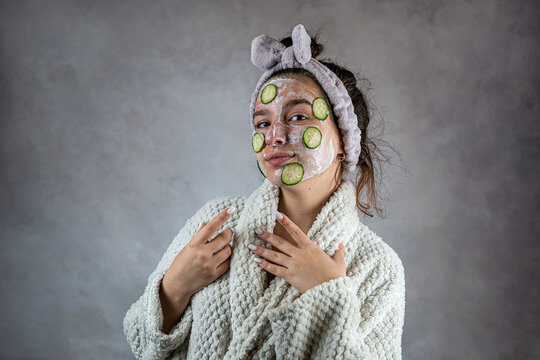 Young woman applying  facial cleanser mask with cream and slices of cucumber