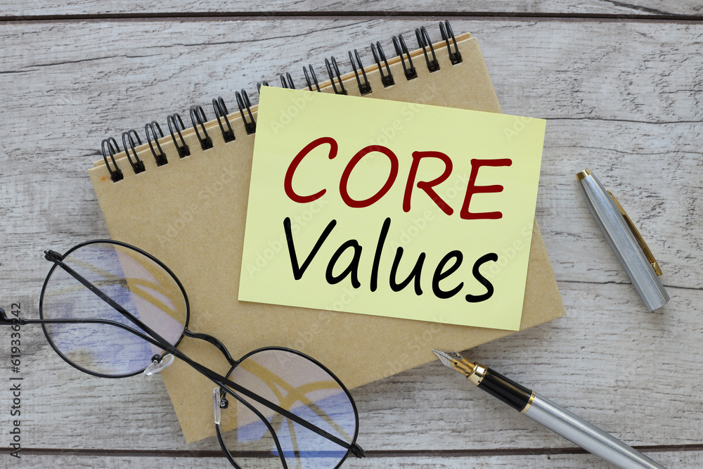 Poster core values text on a yellow sticky note on the desk next to the glasses.