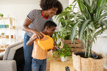 Happy young woman with son watering plants at home